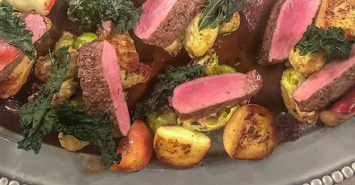 Vildsvinskött med perfekt rosa temperatur, serverat med rostade potatisar, brysselkål och grönkål i en mustig sås.