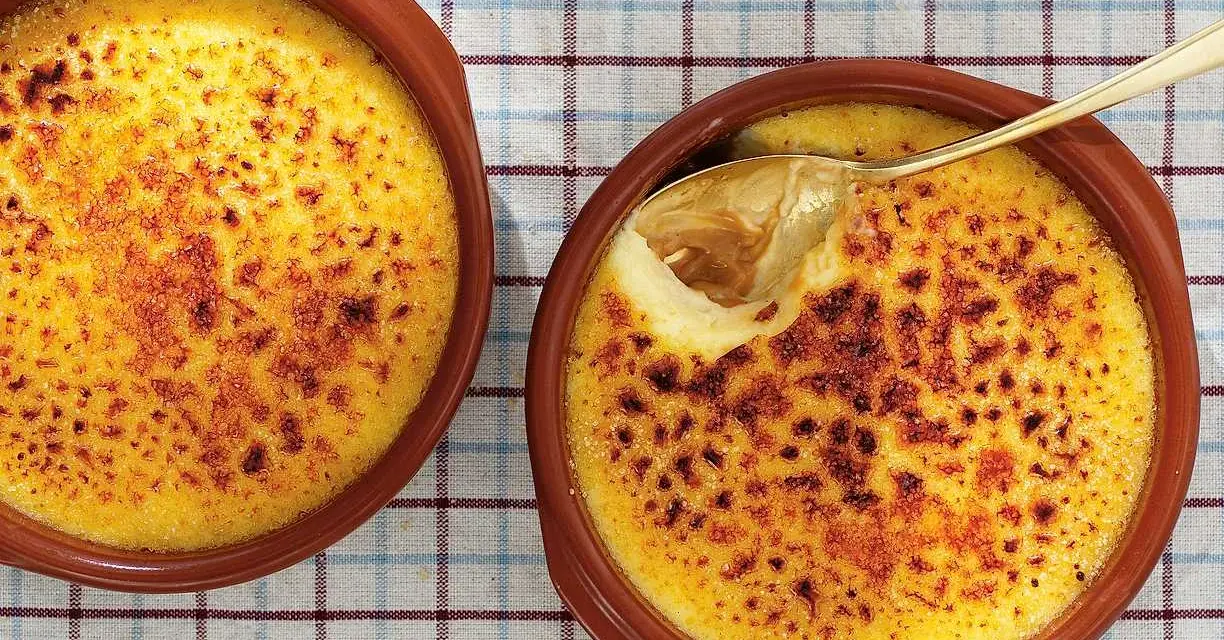 Två krämiga creme brulee i bruna skålar, en med en gyllene sked som lyfter fram den karamelliserade ytan.