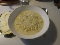 En krämig fänkålssoppa med potatis serveras i en vit skål, bredvid en bit rostat bröd med ost.