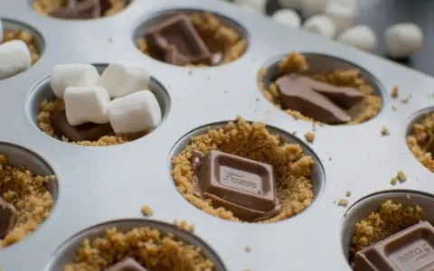 S'mores i ugn förbereds i en muffinsform med krossade kex, chokladbitar och marshmallows.