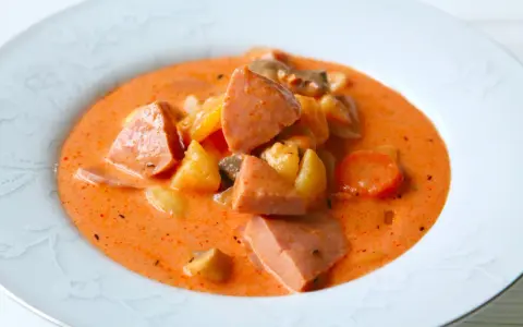 A hearty bowl of korvsoppa with sausage, potatoes, and carrots in a creamy orange broth.