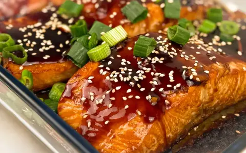 Saftiga filéer av asiatisk lax, glaserade med en mörk sås, toppade med sesamfrön och färsk salladslök.