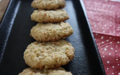 Fredriks fika: en rad hembakade havrekakor på en svart plåt, bredvid en prickig duk.