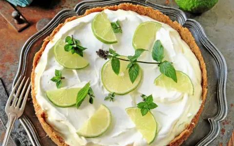 En krämig key lime pie med limeklyftor och mynta på en krispig botten, serverad på ett vackert fat.