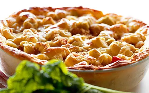 En gyllene, gammaldags rabarberpaj med smuldeg, redo att avnjutas. Framför syns färska rabarberblad.