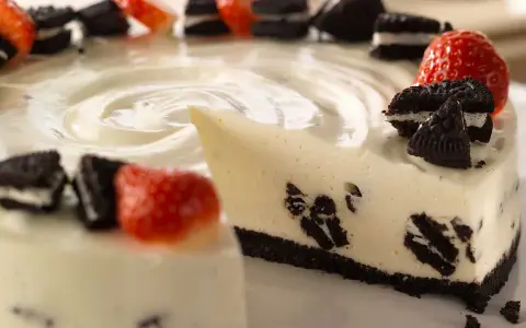 En krämig oreo cheesecake med färska jordgubbar och oreokex som dekoration. En bit är uppskuren.