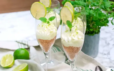 Key lime pie in glasses with whipped cream, lime slices, and mint.