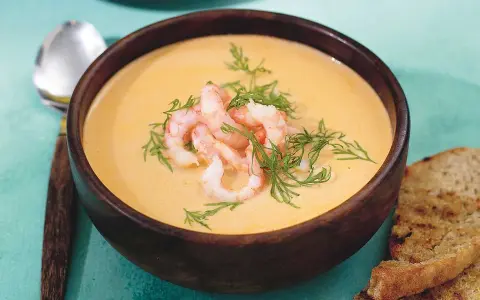 En krämig soppa med räkor och dill, serverad i en träskål med rostat bröd. En härlig soppa med räkor som värmer.