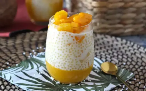 En smaskig mango sago-dessert i ett glas, toppad med färsk mango. En perfekt tropisk njutning.
