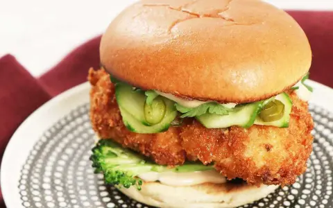 En saftig kyckling hamburgare med krispigt panerat kycklingfilé, gurka, jalapeños och en krämig sås på ett mjukt bröd. Serveras på en snygg tallrik.