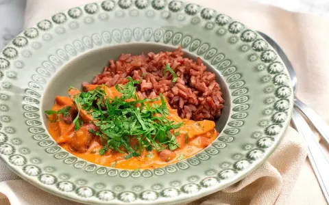 En portion korv stroganoff med rött ris, toppad med färsk persilja, serveras på en vacker grön tallrik.