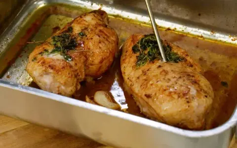 Två saftiga kycklingfiléer med örter i en ugnsform, redo att serveras. Enkel kyckling i ugn som ser utsökt ut.