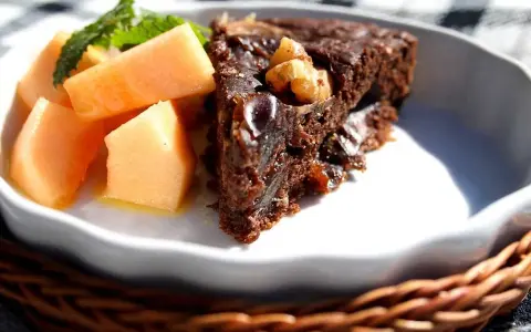 En bit saftig banankaka med choklad och nötter, serverad med färsk melon och mynta.