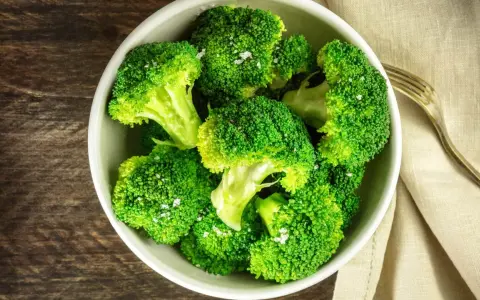 En skål med nykokt, grön broccoli, strödd med flingsalt. En gaffel ligger bredvid på en beige duk.