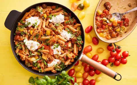 En panna med penne, körsbärstomater, basilika och mozzarella. En härlig vegetarisk mat som ser utsökt ut.