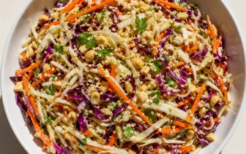 En fräsch asiatisk kålsallad med strimlad vit och rödkål, morötter, jordnötter och sesamfrön.