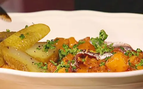 En portion pytt Bellman med stekt potatis, inlagd gurka och ansjovis, toppad med persilja.