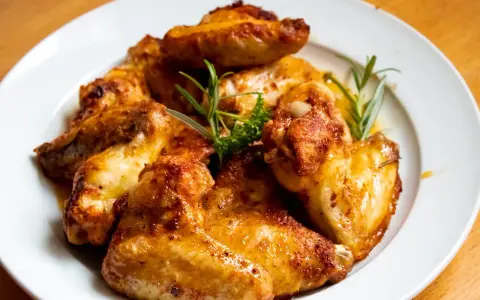 En tallrik med gyllene, grillade kycklingvingar, garnerade med rosmarin. Perfekt för en festmåltid, och med rätt förvaring har grillad kyckling hållbarhet som räcker för att njuta av resterna.