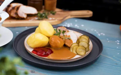 En tallrik med skivad ytterfile i sockerkaksform, potatis, sås, gelé och gurka.