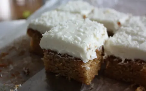 Färska bitar av morotskaka med krämig frosting och kokosflingor. En bit är uppskuren med en kniv.