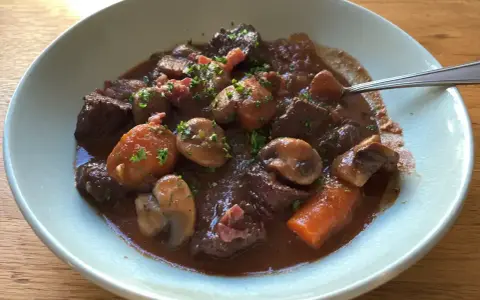 En skål med mustig boeuf bourguignon, fylld med mört kött, champinjoner och morötter, toppad med persilja.