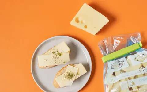 Slices of cheese on bread on a plate, a wedge of cheese, and a bag of cheese chunks.