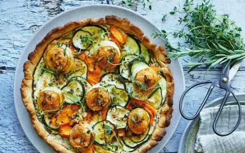 En gyllene, smakrik vegetarisk paj fylld med zucchini, morötter och toppad med ost. Garnerad med färska örter.