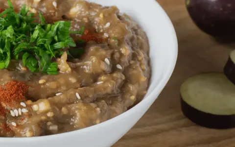 En krämig baba ganoush, toppad med färsk persilja och paprikapulver, bredvid skivade auberginer.