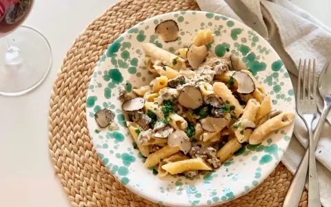 En tallrik med tryffelpasta med svamp och färska örter, serverad på en flätad duk. Ett glas rödvin står bredvid.
