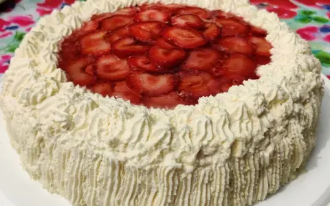 A round cake with whipped cream frosting and sliced strawberries on top.