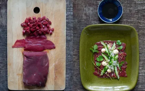 Förberedelser för asiatisk råbiff: rått kött i bitar och skivor på en skärbräda, färdig rätt med gurka, örter och sesamfrön på en grön tallrik.