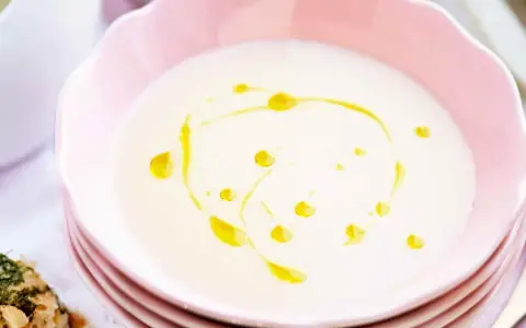 En krämig vit sparrissoppa med en virvel av olivolja i en rosa skål. Serveras med ett kryddigt bröd.
