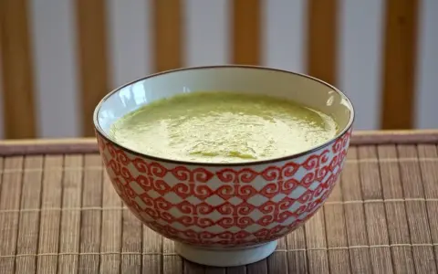 En skål med krämig blomkål och broccolisoppa, serverad på en bambumatta.
