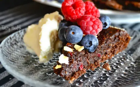 En bit nyttig kladdkaka med bär och grädde på ett mönstrat fat.