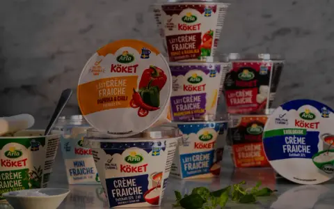 Various Arla Köket crème fraîche tubs, some open, with herbs and a bowl of salt.