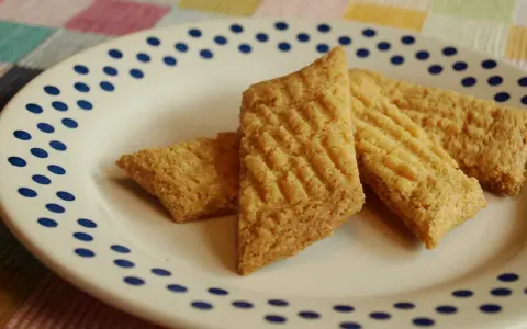 Tre gyllene glutenfria kolakakor ligger på en vit tallrik med blå prickar. De har ett rutmönster på ovansidan.