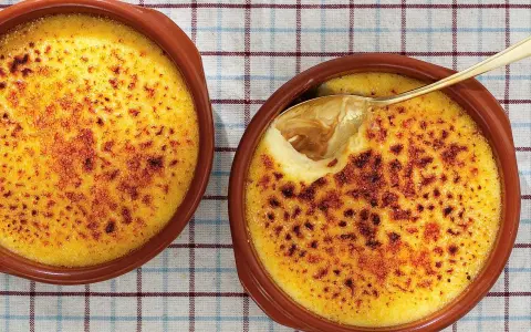 Två krämiga creme brulee i bruna skålar, en med en gyllene sked som lyfter fram den karamelliserade ytan.