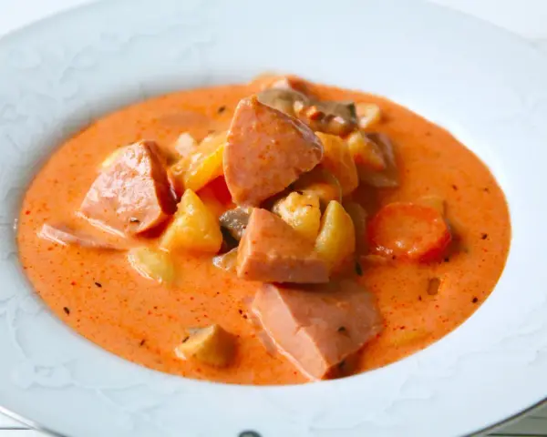 A hearty bowl of korvsoppa with sausage, potatoes, and carrots in a creamy orange broth.