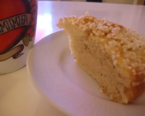 En bit saftig sockerkaka med kardemumma, toppad med nötter, ligger på en vit tallrik bredvid en mugg med texten "MAMMA".