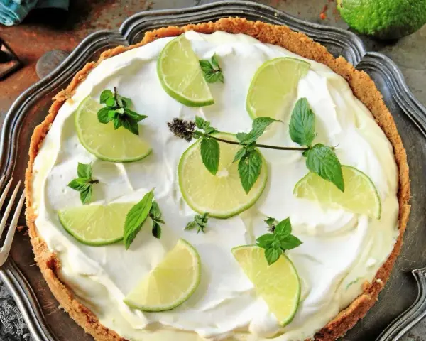 En krämig key lime pie med limeklyftor och mynta på en krispig botten, serverad på ett vackert fat.