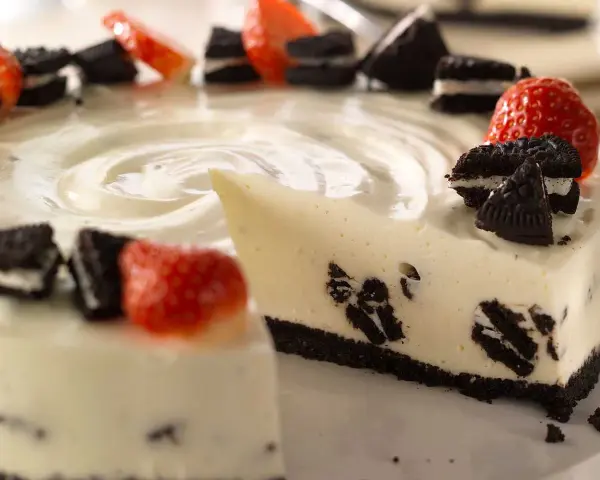 En krämig oreo cheesecake med färska jordgubbar och oreokex som dekoration. En bit är uppskuren.