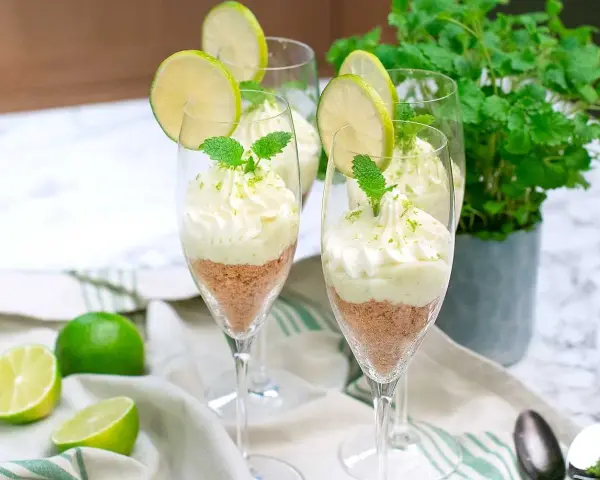 Key lime pie in glasses with whipped cream, lime slices, and mint.