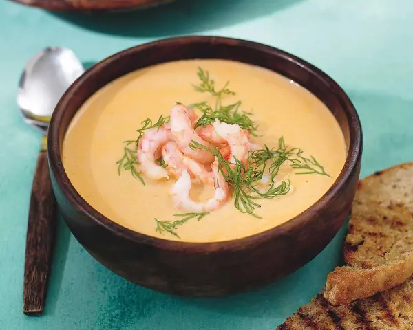 En krämig soppa med räkor och dill, serverad i en träskål med rostat bröd. En härlig soppa med räkor som värmer.