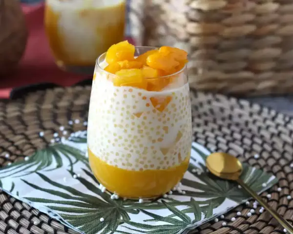 En smaskig mango sago-dessert i ett glas, toppad med färsk mango. En perfekt tropisk njutning.