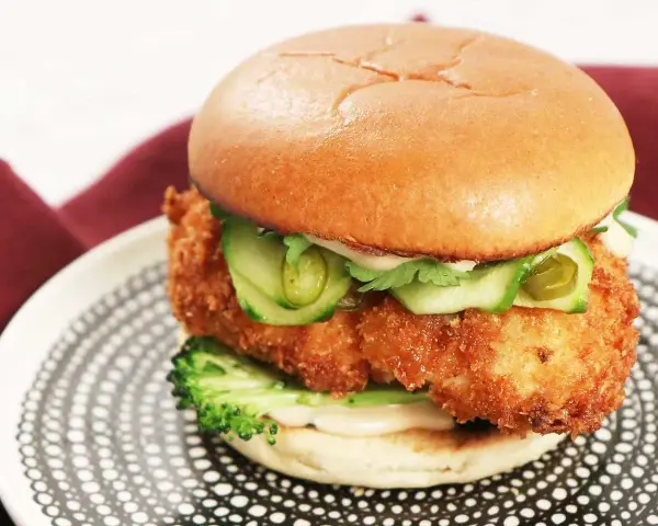 En saftig kyckling hamburgare med krispigt panerat kycklingfilé, gurka, jalapeños och en krämig sås på ett mjukt bröd. Serveras på en snygg tallrik.