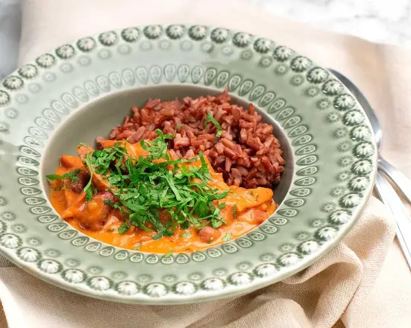 En portion korv stroganoff med rött ris, toppad med färsk persilja, serveras på en vacker grön tallrik.