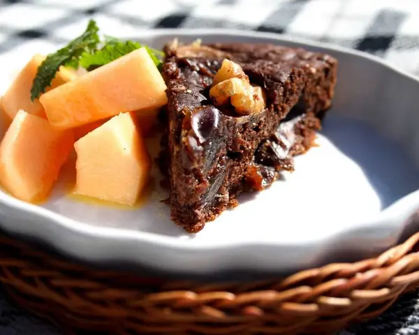 En bit saftig banankaka med choklad och nötter, serverad med färsk melon och mynta.