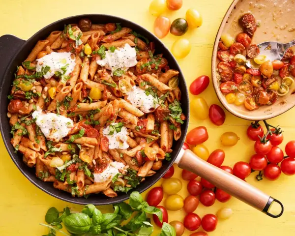 En panna med penne, körsbärstomater, basilika och mozzarella. En härlig vegetarisk mat som ser utsökt ut.