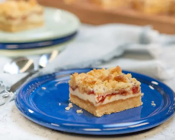A slice of rhubarb cheesecake with a crumb topping on a blue plate.