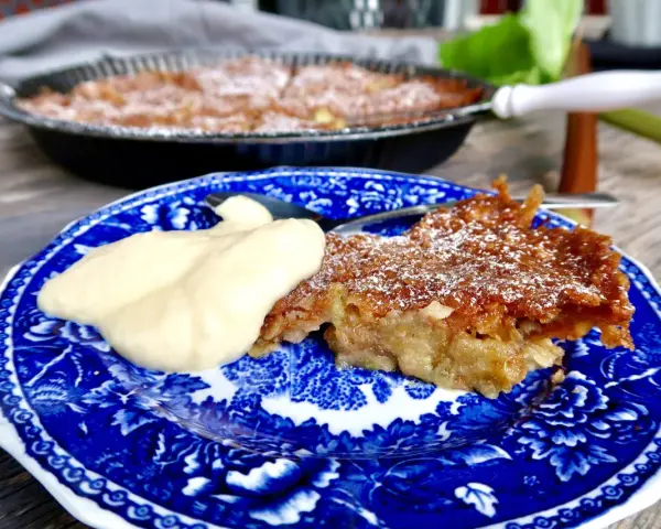 A slice of rhubarb pie with a dollop of cream on a blue and white patterned plate.